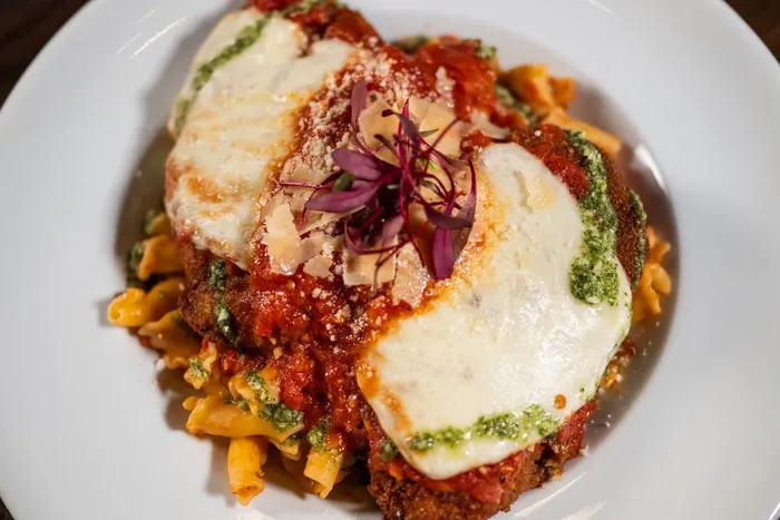 Chicken parmigiana over pasta with pesto drizzle